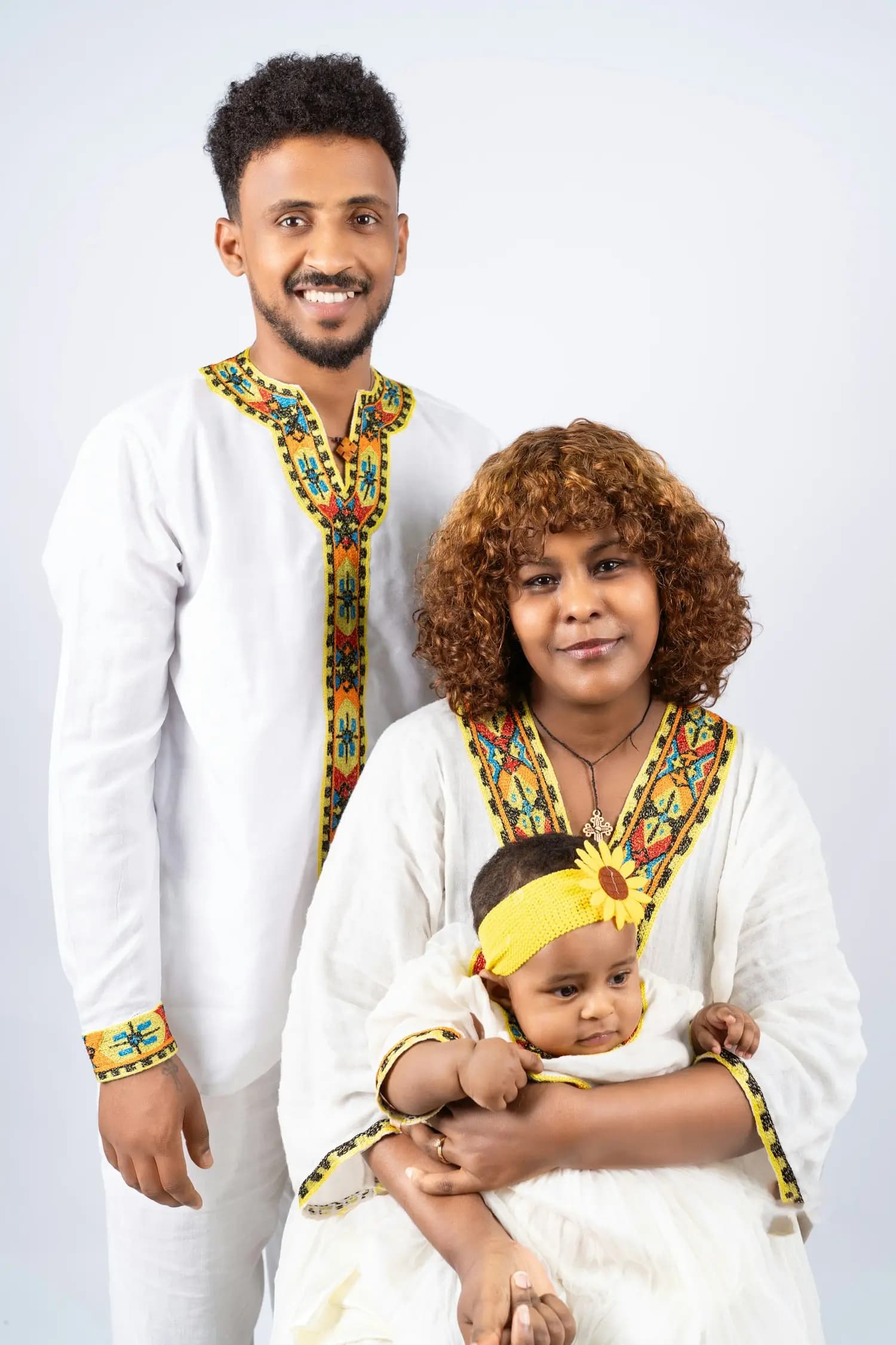 A father, a mother and their baby in white traditional clothing