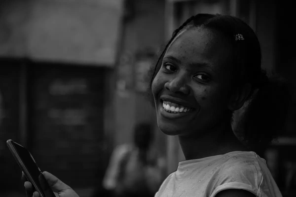 Une jeune femme sourit, son téléphone à la main