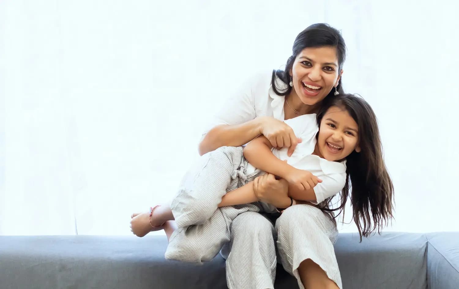 A mother and her daughter laughing on a sofa