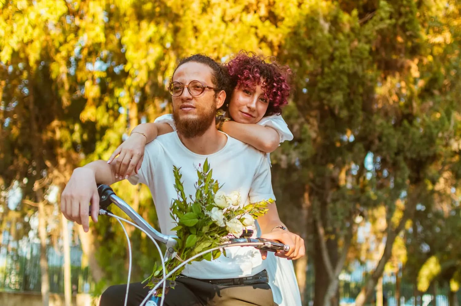 A couple on a bicycle holding a bouquet of flowers
